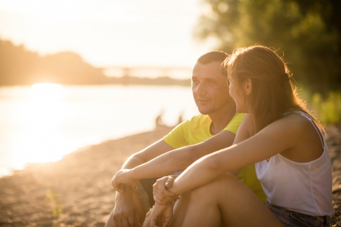 Mann und Frau bei einem intimen Gespräch bei Sonnenuntergang an einem Fluss.