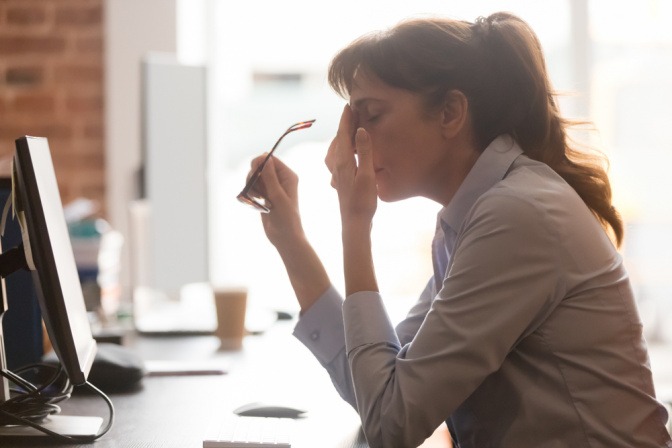 Burnout am Arbeitsplatz - gestresste Frau am Schreibtisch.