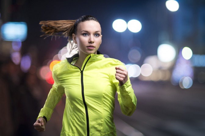 Frau mit neongrüner Jacke beim Joggen im Dunkeln.