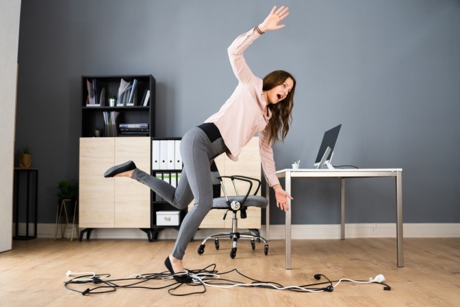 Frau fällt über freiliegende Kabel in ihrem Homeoffice.