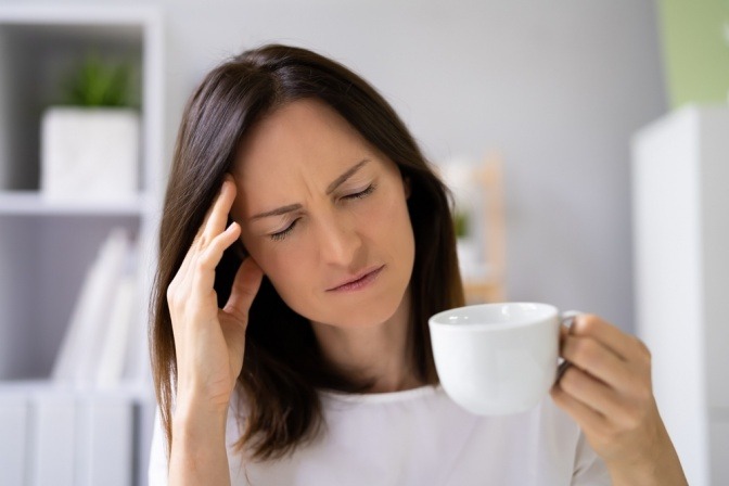 Frau mit Kopfschmerzen hält Tasse mit Kaffee