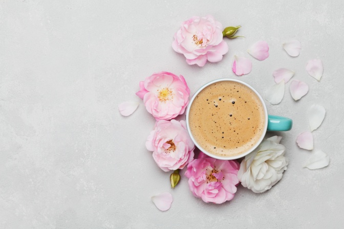 Neben einer Kaffeetasse mit Inhalt liegen Kaffeebohnen