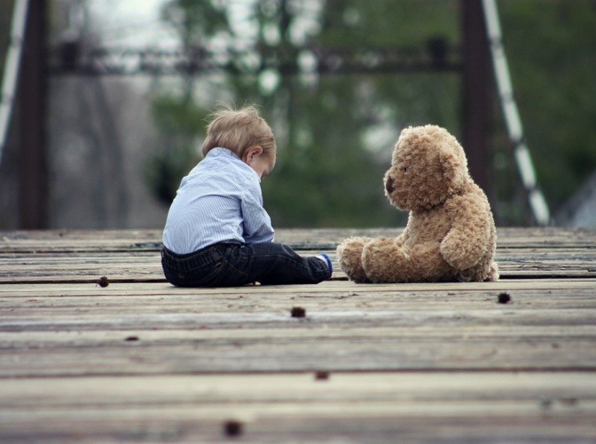 Ein Kind sitzt neben einem Teddybär