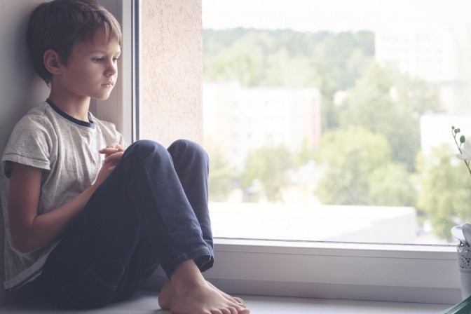 Ein Kind sitzt traurig am Fenster