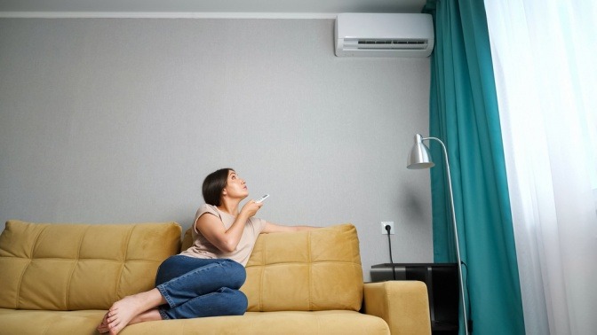 Frau bedient Klimaanlage mit einer Fernbedienung gegen hohe Luftfeuchtigkeit