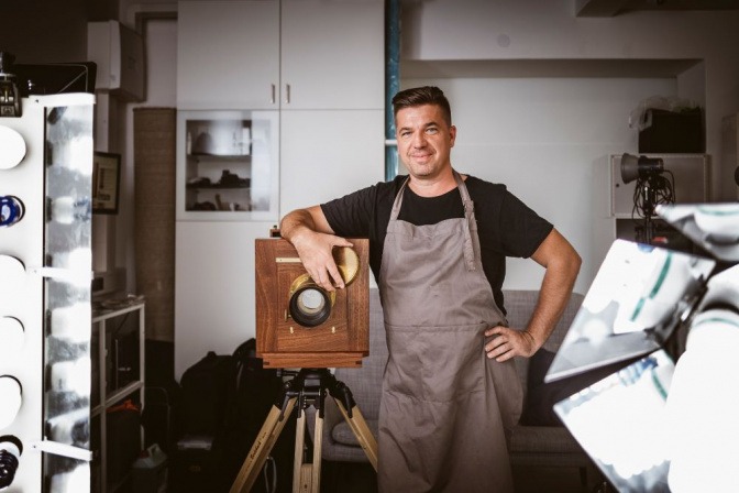 Der Fotograf Erik Diewald steht neben einer Großformatkamera aus Holz
