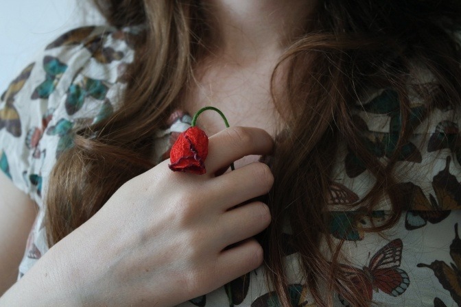 Eine Frau hält eine verwelkte und geknickte Rose vor ihrem Bauch. 