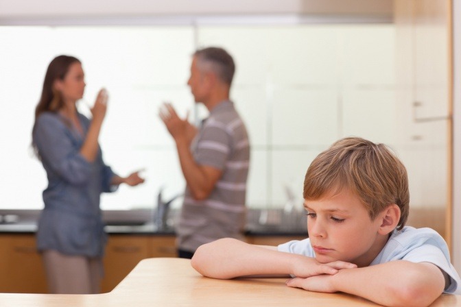 Eine Frau und ein Mann streiten in der Küche, ein Kind sitzt davor