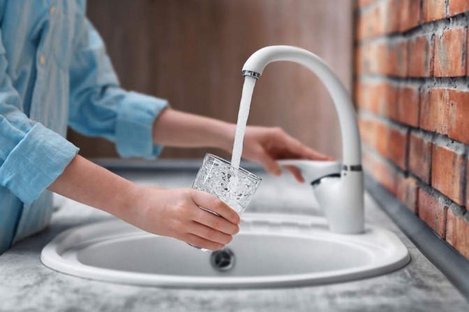 Frau füllt Glas unter Wasserhahn.