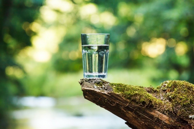 Wasserglas auf einem Stein mit Fluss im Hintergrund.