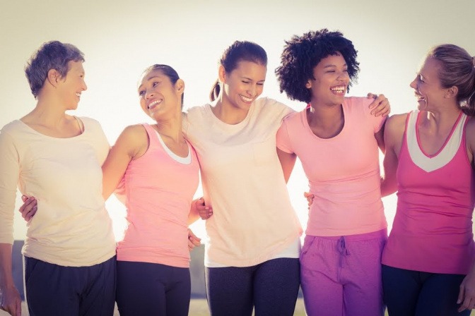 Fünf Frauen, die offensichtlich miteinander befreundet oder zumindest bekannt sind, stehen nebeneinander vor einem Brückengeländer. Hinter ihnen geht die Sonne über dem Meer unter.