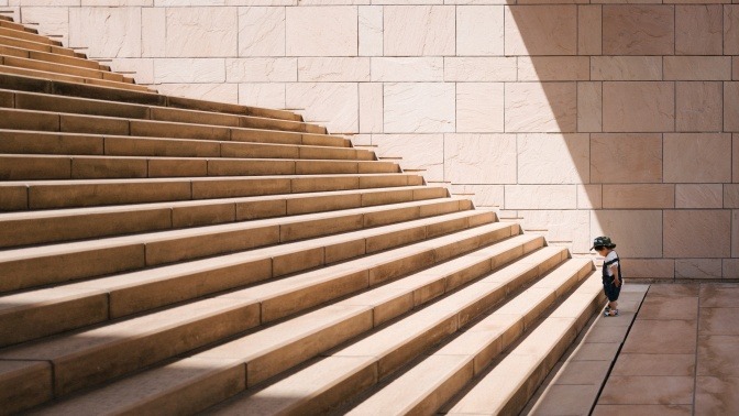 Ein kleiner Junge, der vielleicht auf der Suche nach seinem Lebenssinn ist, steht am unteren Absatz einer großen Treppe.