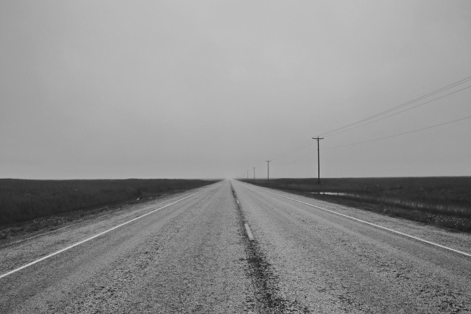 Ein Ausblick auf einer gerade und leere Straße mitten im Nirgendwo, die sich endlos in den Horizont erstreckt.