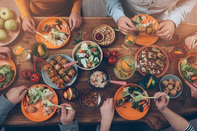 Mehrere Menschen sitzen gemeinsam beim Essen. Die Tafel ist reichhaltig gedeckt. Es fällt jedoch auf, dass es sich um viele unterschiedliche Speisen in kleinen Mengen handelt, statt um eine großes Hauptgericht mit einer oder zwei Beilagen.