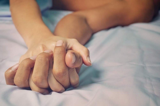 Zwei Hände halten sich im Bett