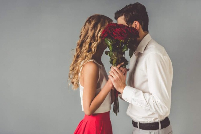 Verliebtes Paar küsst sich hinter Rosenstrauss.