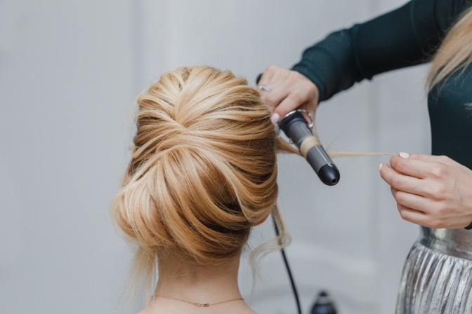 Eine Friseurin setzt den Lockenstab an einer klassischen Hochsteckfrisur an