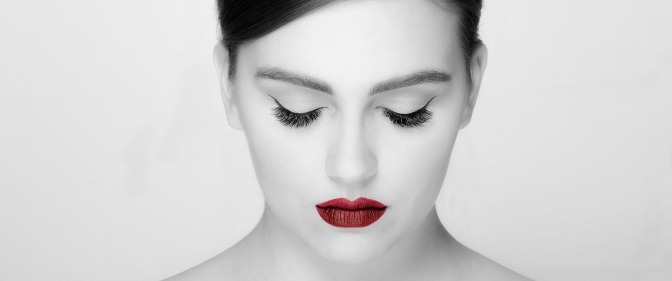 Eine Frau in schwarz-weiß mit roten Lippen hält die Augen zu und trägt Luxuslashes