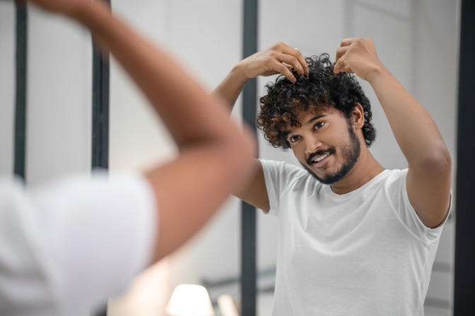 Ein Mann betrachtet und stylt seine lockigen Haare vor einem Spiegel
