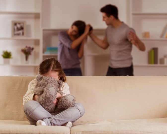 Ein Mann will auf eine Frau schlagen, ein Kind sitzt im Vordergrund mit einem Stofftier