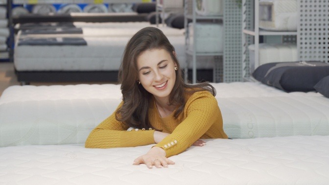 Eine lächelnde Frau legt ihre Hände auf eine Matratze