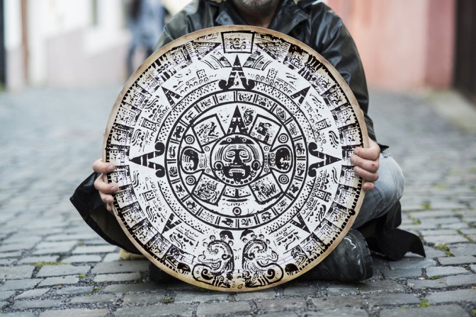 Auf der Straße sitzender Mann hält Maya-Kalender aus Stein