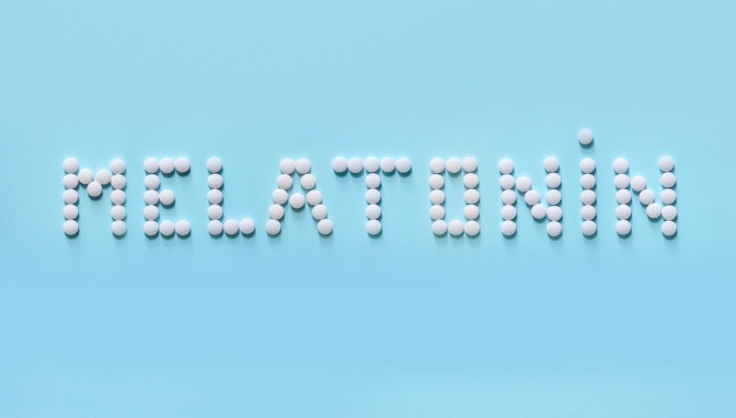Das Wort Melatonin aus weißen Pillen auf blauem Hintergrund