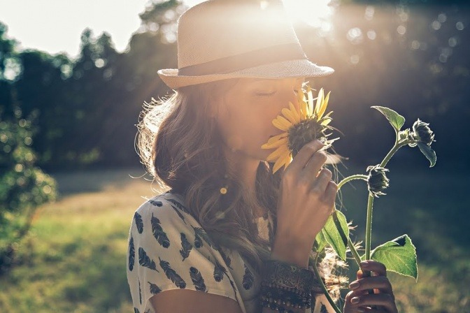 Eine Frau riecht an einem Sommerabend in einem Feld an einer Sonnenblume.