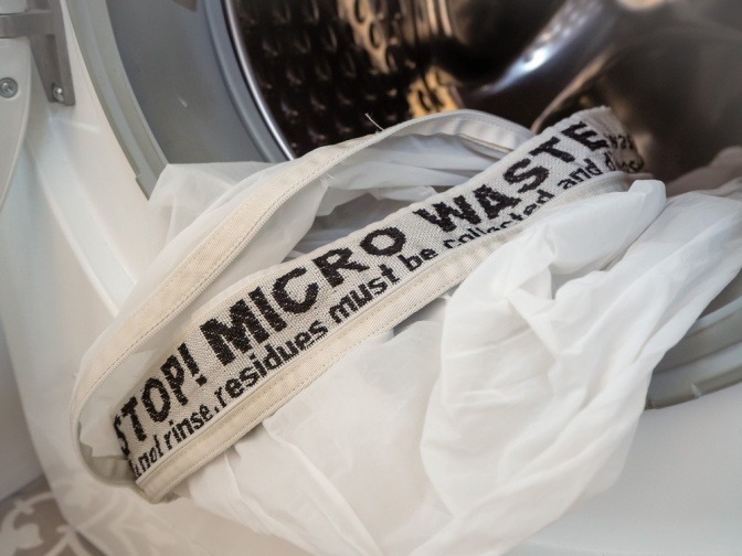 Waschmaschine und Aufdruck auf einem Beutel: "Stop! Micro Waste"
