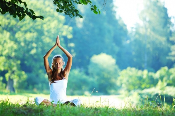 An einem sonnigen Tag macht eine Frau sanfte Entspannungs- und Meditationsübungen in einem Park.
