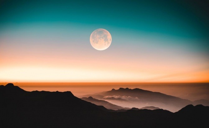 Im Hintergrund einer Berglandschaft befindet sich der Mond