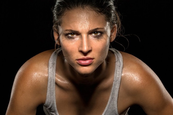 Eine Frau blickt nach einem anstrengenden Training entschlossen und fokussiert in die Kamera.