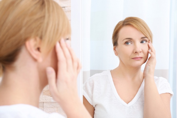 Eine Frau betrachtet im Spiegel ihre müden Augen
