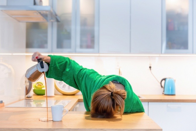 Müde Frau, die beim Frühstück auf dem Tisch in der Küche schläft und Kaffee verschüttet.