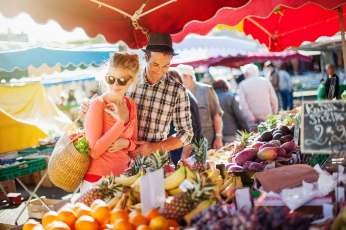 Junges Paar kauft Gemüse von lokalen Produzenten an einem Marktstand.