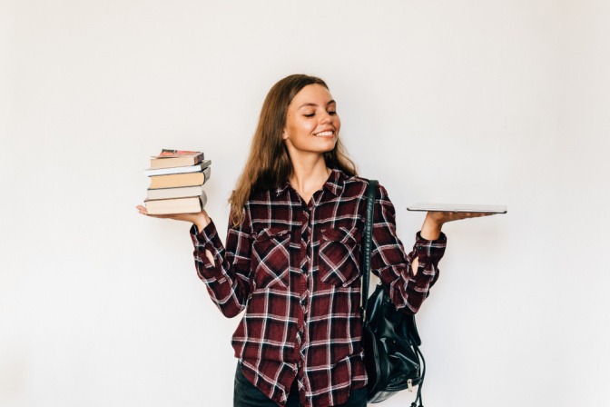Papier versus digital - Frau hält Stapel mit Büchern in der einen und ein einzelnes kleines Tablet in der anderen Hand.