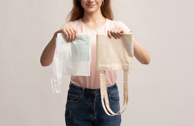 Junge Frau hält Einweg-Plastiktüte in der einen und eine wiederverwendbare Stofftasche in der anderen Hand.