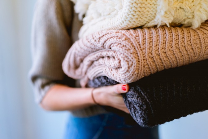 Frau mit einem Stapel Pullover im Arm