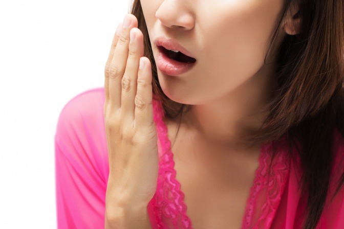 Frau hält Hand vor Mund und testet Mundgeruch