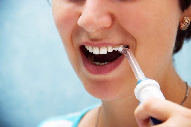 Eine Nahaufnahme einer jungen Frau, die sich die Zähne mit einer Munddusche spült.