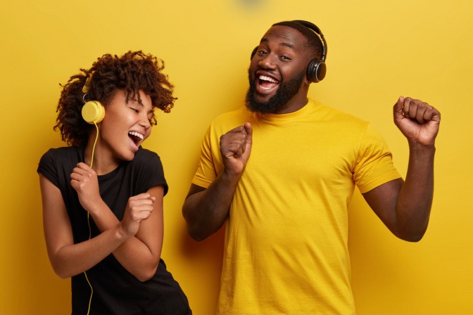 Eine junge Frau und ein junger Mann hören mit Kopfhörern Musik und tanzen fröhlich