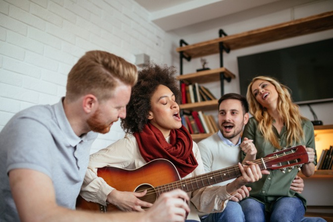 Eine junge Frau spielt Gitarre und singt mit ihren Freunden
