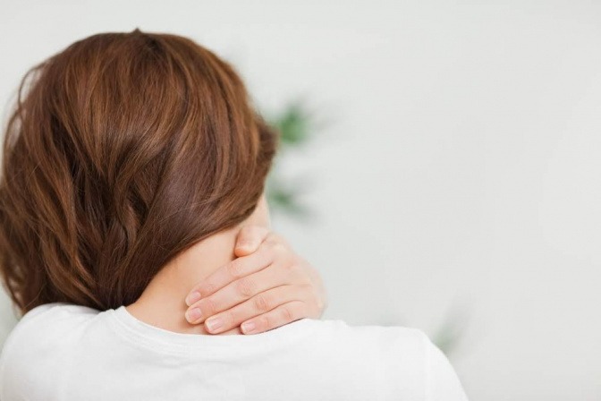 Eine sitzende Frau greift sich mit der Hand an ihren offenbar schmerzenden Nacken.