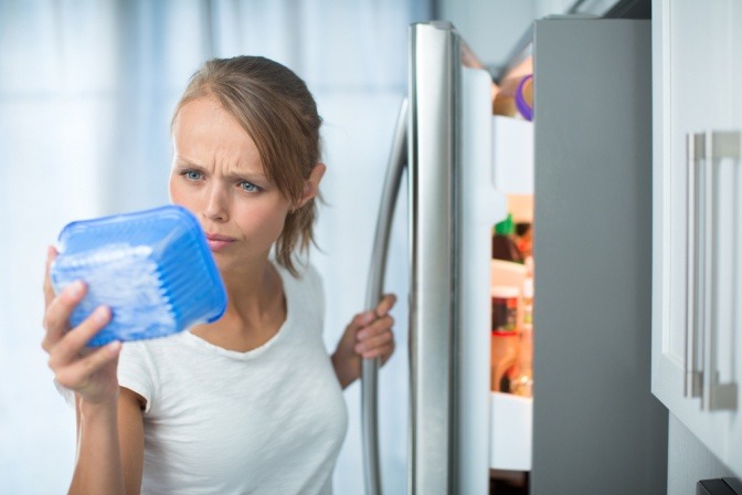Eine Frau checkt das Verfallsdatum einer Schale Champignons, die sie gerade aus dem Kühlschrank genommen hat.