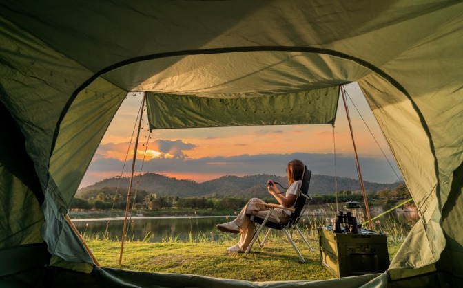 Frau beim Sonnenuntergang vor ihrem Zelt in der freien Natur.