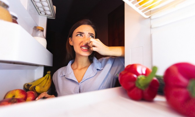Frau öffnet Kühlschrank und verzerrt Gesicht wegen schlechtem Geruch.