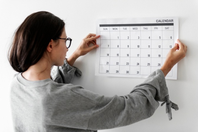 Frau hängt Kalender an die Wand.