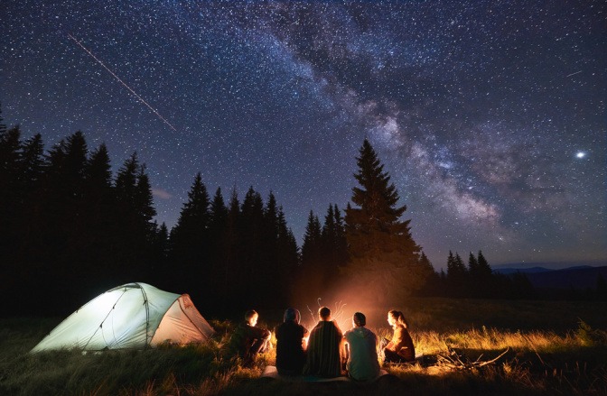 Menschen mit Zelt und Lagerfeuer am Abend mit Neumond im August