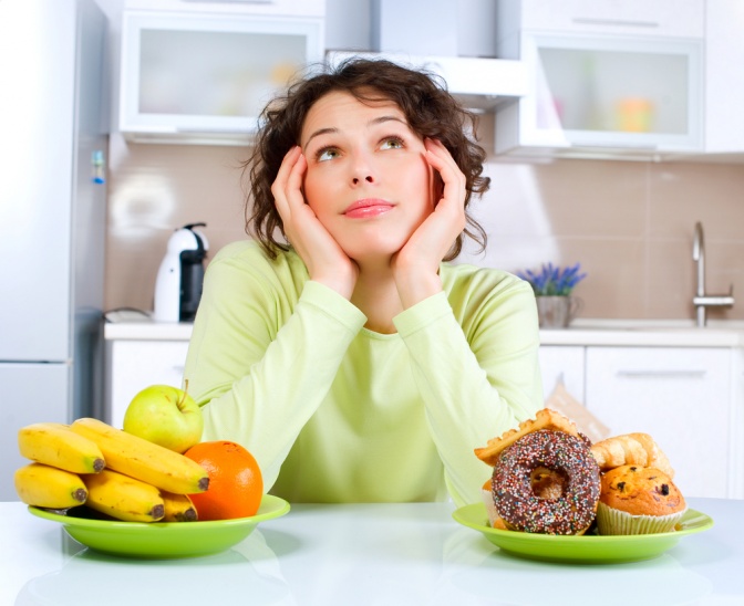 Eine Frau sitzt mit dem Kopf auf die Ellbogen gestützt vor einem Teller mit Obst und einem mit Süßem