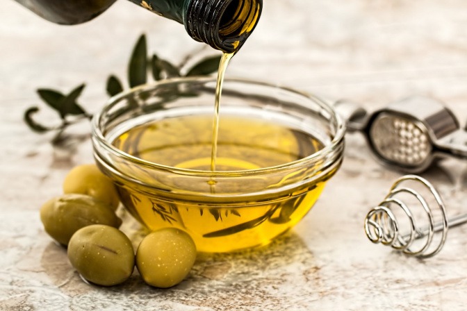 Oliven liegen neben einer Schüssel mit Öl